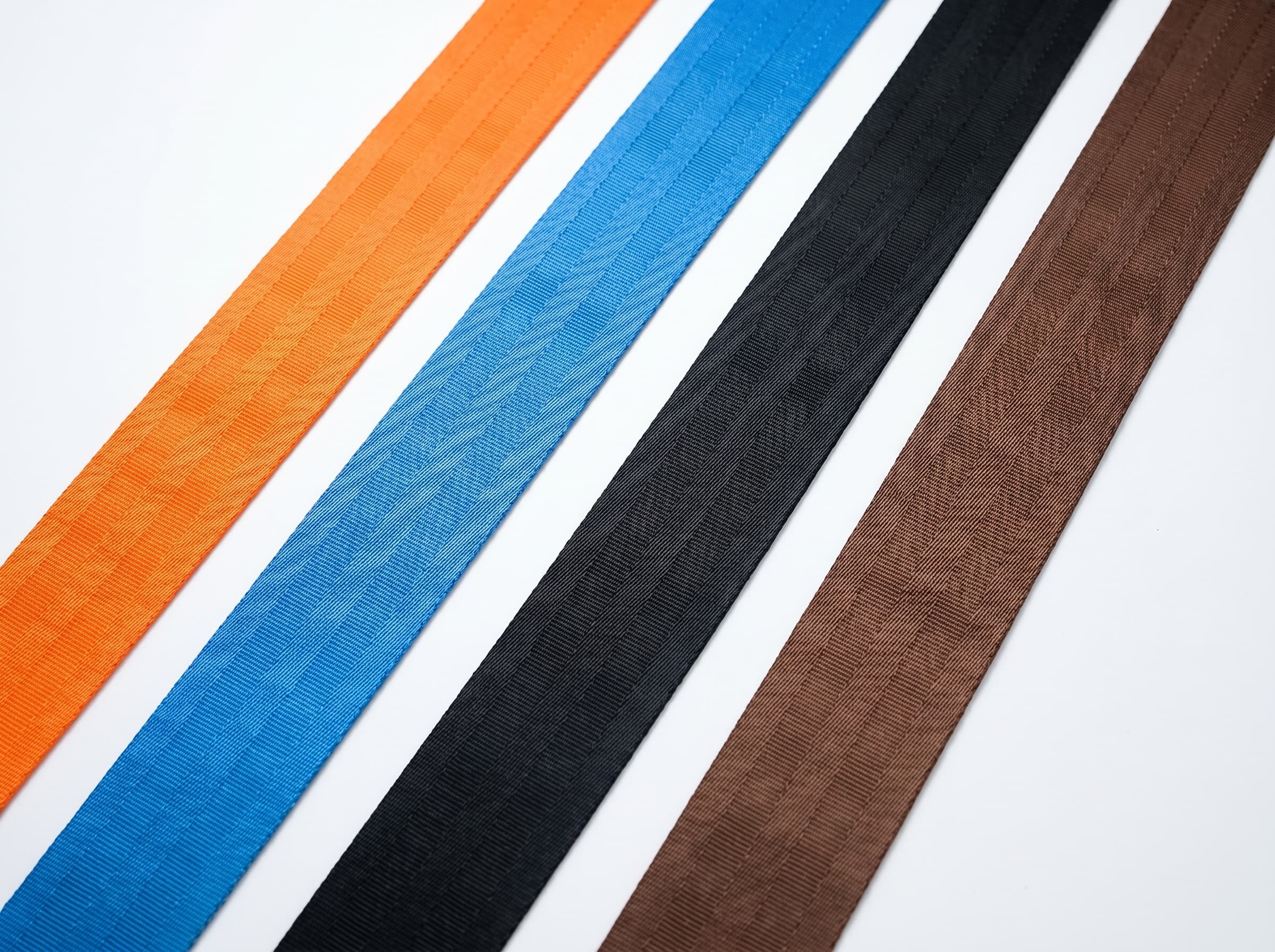 Orange, blue, black, and brown polyester webbing strips on a white studio surface
